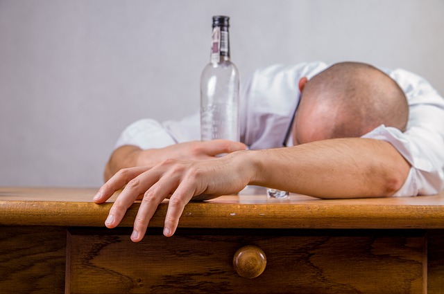 Stock image of a white man slumped over a table with a bottle in his hand