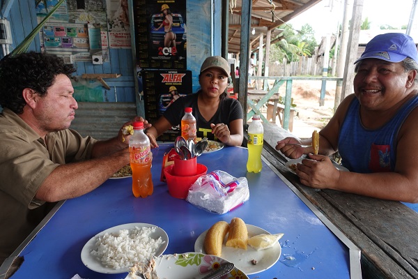 Two men and a woman sit around a table eating rice, plantains, and pork