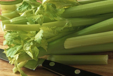 Celery stalks on a cutting board, with a knife ominously lurking underneath